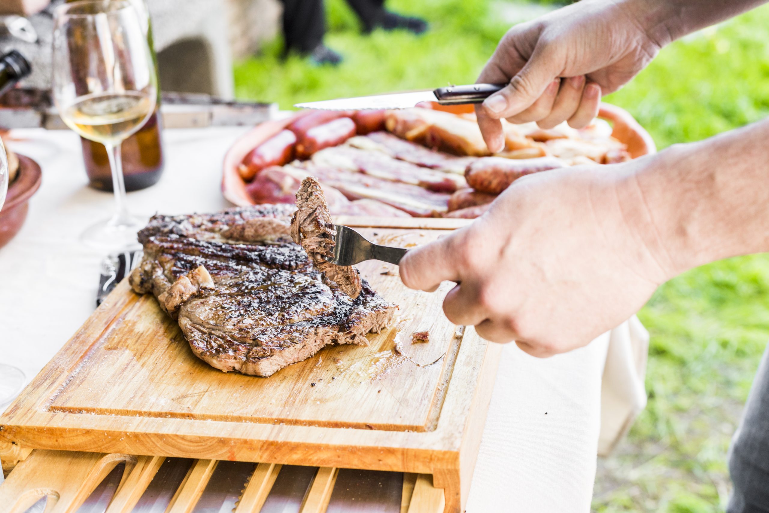 close-up-hand-cutting-fresh-grilled-beef-table-outdoors